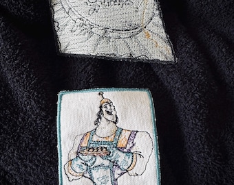 May include: Two embroidered patches. The first patch is white with black embroidery and says "Magical Little Stitchers". The second patch is white with colorful embroidery and shows a cartoon character holding a plate of food. The text below the character says "Spinach Puff?"