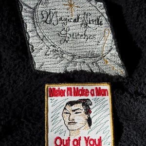 May include: Two embroidered patches. The first patch is white with black embroidery and reads "Magical Needle Stitches". The second patch is white with black and red embroidery and reads "Mister I'll Make a Man Out of You".
