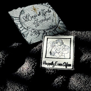 May include: Two embroidered patches on a dark gray fabric background. The first patch is a circle with the text "Magical Circle of Whimsy" in cursive. The second patch is a white rectangle with a black and white illustration of a couple embracing and the text "Happily Ever After".