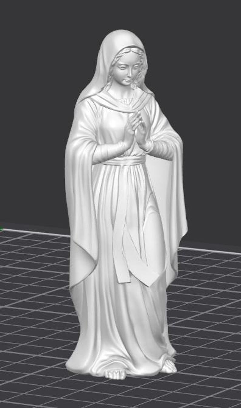 Op de afbeelding: Een wit beeld van een vrouw in een vloeiende jurk en hoofdbedekking, met de handen gevouwen in gebed. De figuur heeft een serene uitdrukking en staat op een oppervlak met een rasterpatroon. Het beeld is een religieuze figuur.