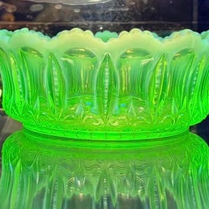 May include: A vibrant lime green opalescent glass bowl featuring a scalloped rim and vertical ribbed detailing. The bowl displays a translucent quality with a milky white edge along the top, showcasing a pressed glass pattern with pointed arches.