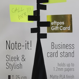 Op de afbeelding: Zwarte plastic business card stand met een gewogen basis voor stabiliteit. Het houdt tot 1,2 mm papier vast en is 25 cm hoog en weegt 200 gram. De stand heeft een notitiehouder met een gele sticky note waarop "CALL HER!!" staat en een groene sticky note waarop "REMIND ME!" staat. Een gouden cadeaukaart wordt ook op de stand weergegeven.