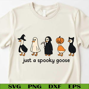 May include: A cream-coloured t-shirt with a Halloween-themed design. It features cartoon geese dressed in costumes: a witch, ghost, grim reaper, pumpkin, and cat. The text "just a spooky goose" is printed below the geese.