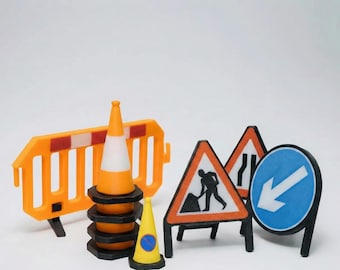 Può includere: Una collezione di segnali stradali e attrezzature di sicurezza per lavori stradali in miniatura. Include coni arancioni e bianchi, una barriera giallo-arancio e vari segnali stradali con grafica in bianco e nero.