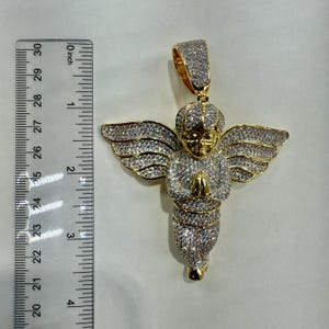 May include: Gold-toned angel pendant with outstretched wings, covered in sparkling stones. The pendant is approximately 2.5 inches long, with a detailed face and clasped hands. The pendant has a bail for a chain.