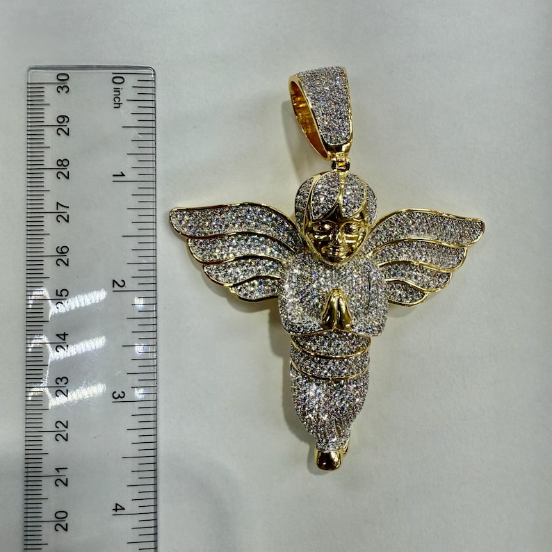 May include: Gold-toned angel pendant with outstretched wings, covered in sparkling stones. The pendant is approximately 2.5 inches long, with a detailed face and clasped hands. The pendant has a bail for a chain.