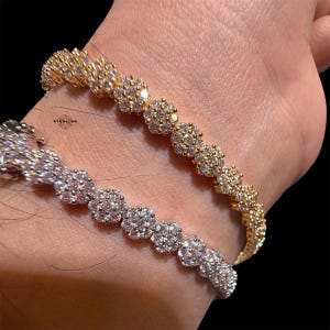 May include: Two tennis bracelets, one gold-toned and one silver-toned, each with a floral design. The bracelets are decorated with many small, sparkling stones. The word "STERLING" is visible on the left bracelet.