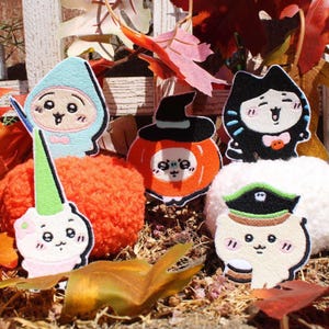 Puede incluir: Parches bordados con temática de Halloween con personajes de dibujos animados disfrazados. Incluye una bruja, un gato, un pirata y un unicornio. Los parches están colocados sobre un fondo de hojas de otoño y una valla de madera.