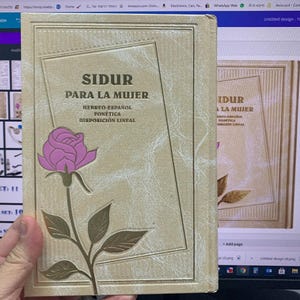 May include: A gold-coloured book with a pink rose design on the cover. The title of the book is "Sidur Para La Mujer" in Spanish, which translates to "Prayer Book for the Woman". The book also includes the text "Hebreo-Español Fonética Disposición Lineal", which translates to "Hebrew-Spanish Phonetic Linear Arrangement".