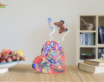 May include: A colorful, abstract heart sculpture with the word "love" written on it. Two butterflies are attached to the top of the sculpture with wire.