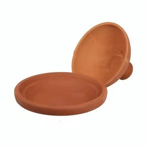 Puede incluir: Un tajine de terracota que consta de una base circular poco profunda y una tapa cónica separada con un pequeño pomo. La arcilla sin esmaltar tiene un color marrón rojizo natural y terroso, con una textura suave y mate en todo el recipiente.