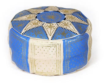 May include: A round floor pouf featuring alternating panels of blue and cream-colored material. The top surface displays a central blue circle with radiating lines, surrounded by star-shaped patterns in blue and cream with black stitching.