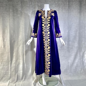 May include: A floor-length, long-sleeved purple velvet dress featuring a deep slit neckline and intricate gold floral embroidery running vertically down the center front, along the neckline, and around the sleeve cuffs.