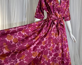 May include: A floor-length wrap dress featuring a vibrant floral pattern in shades of magenta, pink, and orange. The garment has a notched collar, three-quarter length sleeves, and a matching fabric tie belt that cinches at the waist.