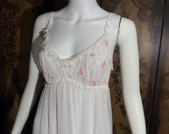 May include: A white sleeveless nightgown featuring a sheer mesh overlay with delicate pink floral embroidery and green leaf accents. The bodice includes a V-neckline trimmed with intricate lace detailing and thin shoulder straps.