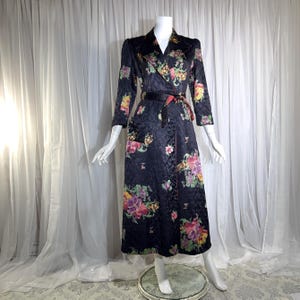 May include: A long-sleeved, floor-length quilted robe in black featuring a vibrant floral print with shades of pink, yellow, purple, and green. The robe includes a notched collar, a matching tie belt at the waist, and a single visible pocket.