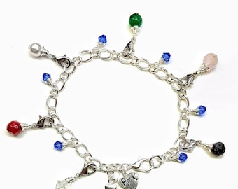 May include: A silver charm bracelet with a heart charm engraved with "PMK" and various charms including a white pearl, red, green, and pink stones, blue crystals, and a black lava rock.