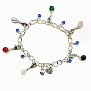May include: A silver charm bracelet with a heart charm engraved with "PMK" and various charms including a white pearl, red, green, and pink stones, blue crystals, and a black lava rock.