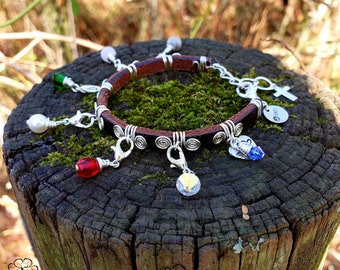 May include: A brown leather bracelet with silver charms, including a cross, a heart, and a swirl design. The bracelet has a variety of colorful beads, including red, green, white, and blue.