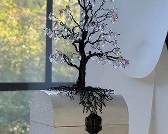 May include: A white wooden box with a black metal latch and a wire tree sculpture with iridescent glass beads. The tree is rooted in the box and has a black wire base.