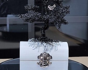 May include: A handcrafted sculpture of a wire tree with a small silver bird perched in its branches. The tree sits atop a light blue wooden chest with a silver clasp. The tree's roots are painted on the chest.