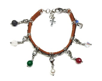 May include: A brown leather bracelet with multiple charms, including a cross, a heart, a crystal, and various colored beads.