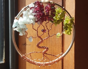 May include: A copper wire tree of life with a silver circular frame. The tree is decorated with green, red, and blue gemstones.