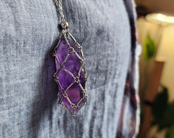 May include: A silver chain necklace with a purple amethyst crystal encased in a silver wire cage pendant.