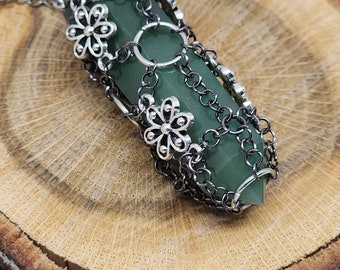 May include: A green gemstone pendant wrapped in a black chain with silver flower accents.