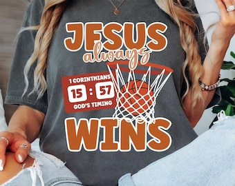 May include: A gray t-shirt with the text "JESUS always WINS" in orange. The shirt also features a basketball hoop with a basketball in it and the text "1 Corinthians 15:57 GOD'S TIMING".