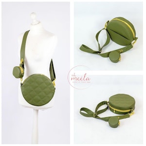 Puede incluir: Un bolso de hombro redondo acolchado verde con una cremallera dorada y una pequeña bolsa redonda a juego. El bolso tiene una correa larga ajustable.