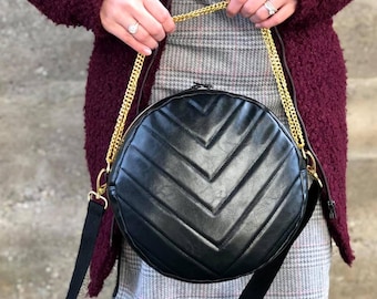 May include: A black round crossbody bag with a gold chain strap and a quilted chevron pattern.