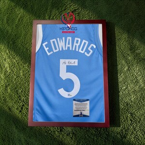 May include: A framed light blue jersey with the name "EDWARDS" and the number "5" in white. The jersey is signed and includes a certificate of authenticity. The frame is a dark brown color.