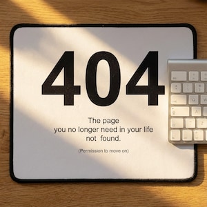 May include: White rectangular mousepad with the number "404" in large black font. Below, the text reads "The page you no longer need in your life not found. (Permission to move on)." A silver keyboard is partially visible.
