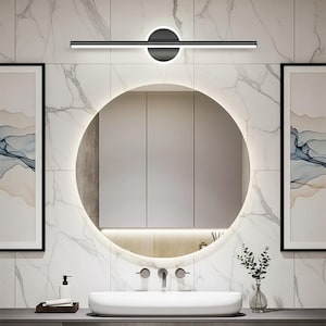 Peut inclure: Salle de bain moderne avec un miroir rond éclairé au-dessus d'un lavabo blanc. Un luminaire noir et argenté élégant est monté au-dessus du miroir. Les murs sont recouverts de carreaux à motifs de marbre, avec des œuvres encadrées de chaque côté.