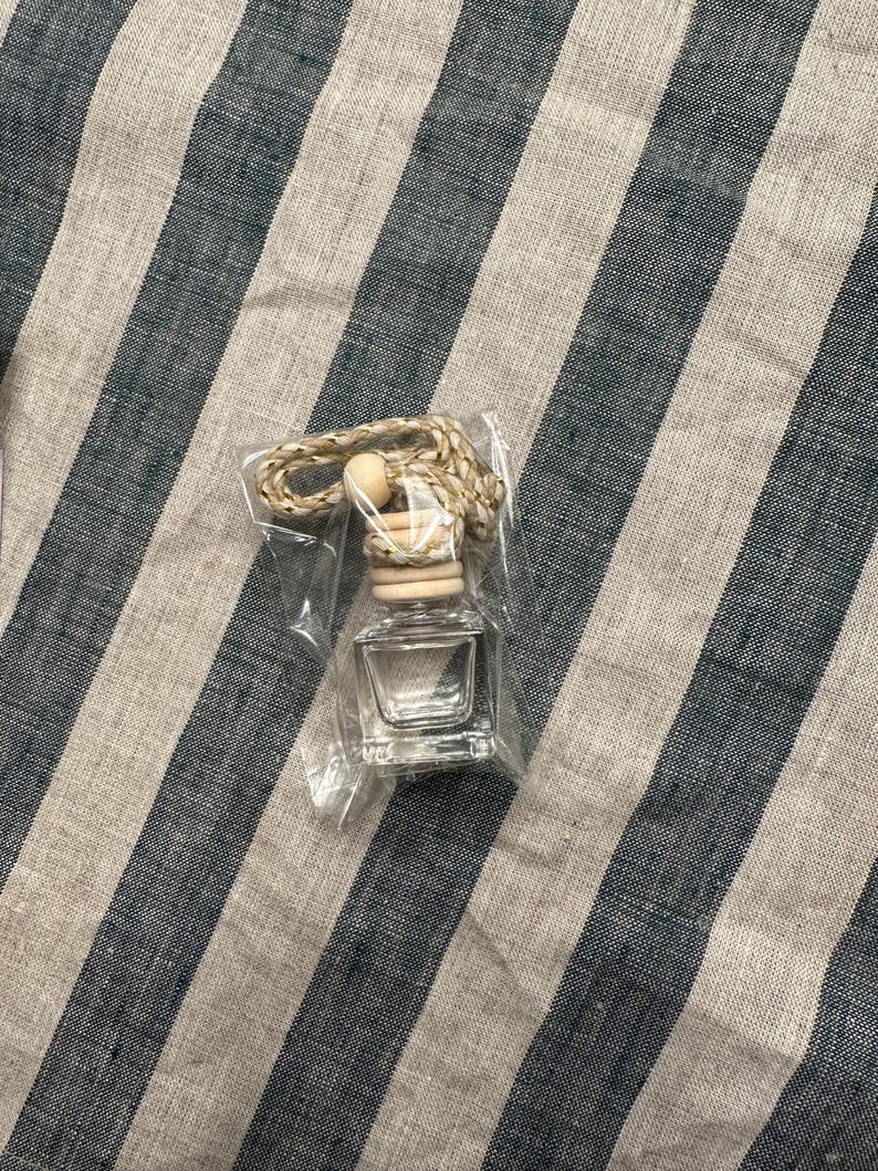 K&ouml;nnte beinhalten: Eine kleine, durchsichtige Glasflasche mit einem Holzstopfen und einer daran befestigten Schnur. Die Flasche ist in einer durchsichtigen Plastikt&uuml;te verpackt.