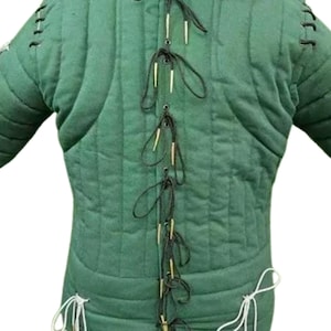 May include: Green padded gambeson with quilted construction. The medieval garment features vertical stitching and is laced up the back with black and white cords. The sleeves are long and the garment is designed to be worn as a protective layer.