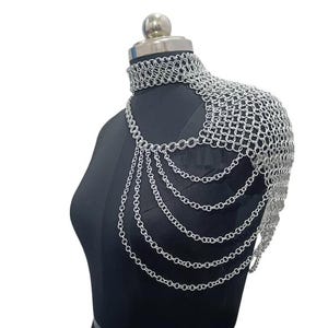 Puede incluir: Armadura de hombro de cota de malla plateada exhibida en un maniquí negro. La armadura presenta un cuello tipo gargantilla, cobertura de hombros y múltiples cadenas colgantes. El metal tiene un acabado brillante y reflectante, y el diseño es intrincado.