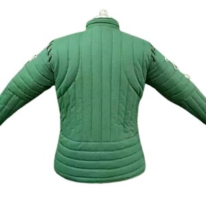 May include: Green padded jacket with long sleeves, likely for historical reenactment or costume use. The jacket has a quilted design with vertical and horizontal stitching, and decorative stitching on the sleeves. The collar is a stand-up style.