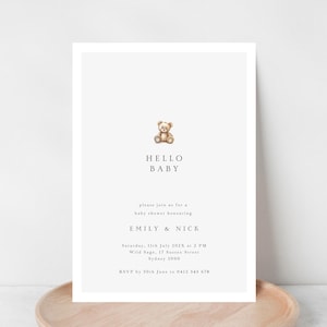Pode incluir: Um convite para chá de bebé com um design minimalista. O convite apresenta uma pequena ilustração de um ursinho de pelúcia no topo, com as palavras "HELLO BABY" abaixo. O convite inclui os nomes dos futuros pais, data, hora e local.