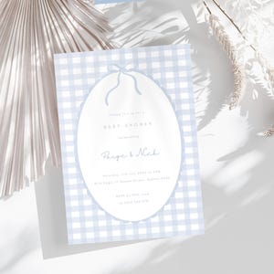Pu&ograve; includere: Invito per baby shower con sfondo a motivo gingham azzurro chiaro. L'invito presenta una forma ovale con un disegno a fiocco nella parte superiore. Il testo recita "Baby Shower" e i nomi "Paige & Nick".