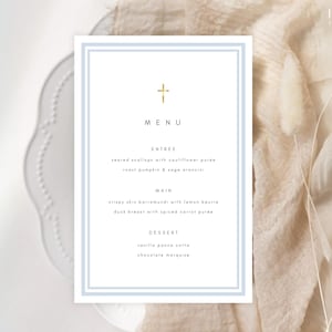 Może przedstawiać: Karta menu z jasnoniebieską obwódką i złotym krzyżem na górze. Słowo "MENU" jest wyśrodkowane, z daniami z przystawki, dania głównego i deseru wymienionymi poniżej. Karta znajduje się na białym talerzu.