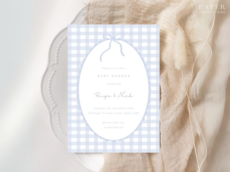 Pu&ograve; includere: Un invito per un baby shower con uno sfondo a quadretti vichy azzurri. L'invito presenta una cornice ovale con un bordo smerlato e un fiocco in alto. Il testo recita "Baby Shower" e i nomi "Paige & Nick".