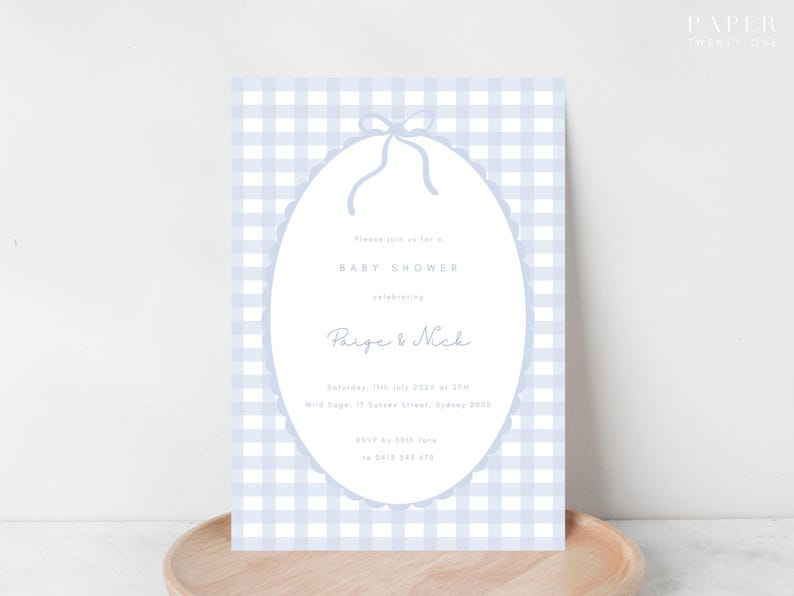 Pu&ograve; includere: Invito per baby shower con sfondo a quadretti vichy azzurri. L'invito presenta una cornice ovale con bordo smerlato e fiocco. Il testo include "Baby Shower" e i nomi "Paige & Nick".
