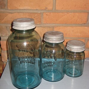 May include: Three blue glass jars with silver lids. The jars are different sizes and have a vintage look. The jars are on a gray surface.