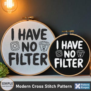 May include: Two embroidery hoops with black and white cross stitch patterns. The white hoop has a black design that says "I HAVE NO FILTER" with a camera and a coffee cup. The black hoop has a white design that says "I HAVE NO FILTER" with a camera and a coffee cup.