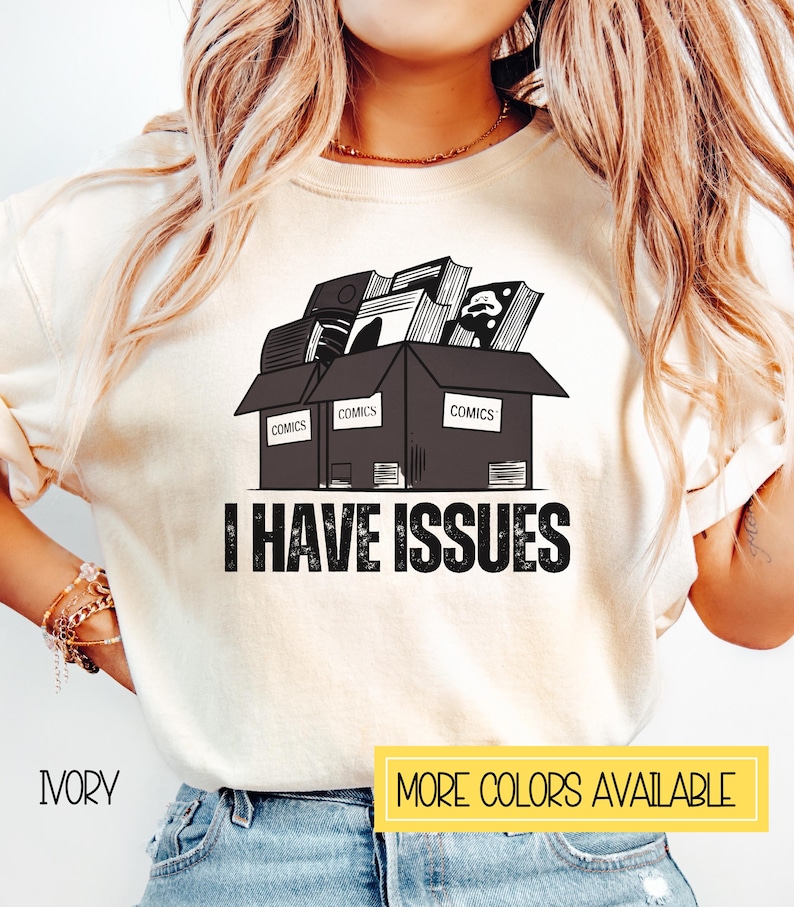 May include: A white t-shirt with a black and white graphic of a box overflowing with comic books. The box has the word "COMICS" printed on each side. The text "I HAVE ISSUES" is printed below the box.