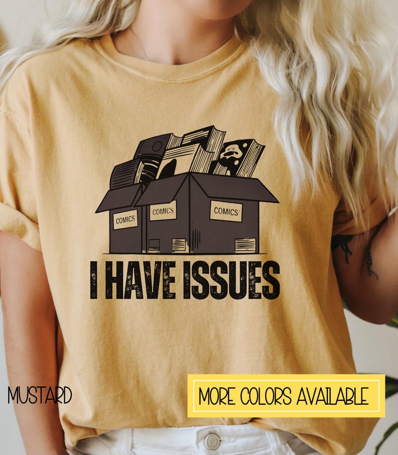 May include: A mustard yellow t-shirt with a graphic of a box overflowing with comic books. The box is labeled "COMICS" on each side. The text "I HAVE ISSUES" is printed below the box.