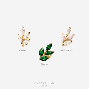 May include: Three gold leaf-shaped earrings with different colored stones. The earrings are set with clear, green, and rainbow stones.