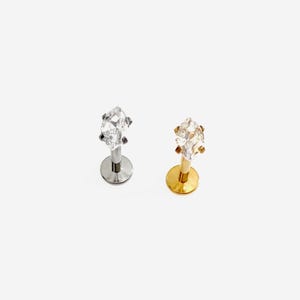 May include: Two labret body jewellery pieces with flat circular bases and marquise-cut clear gemstones. One piece features a silver-toned metal post and setting, while the other piece features a gold-toned metal post and setting.